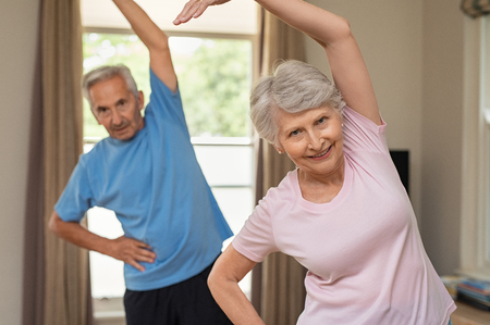 Portrait of happy smiling senior couple with arms raised doing stretching exercise at home. Old man and elderly woman practicing at home during early morning. Retired couple doing aerobics workout indoor.の写真素材