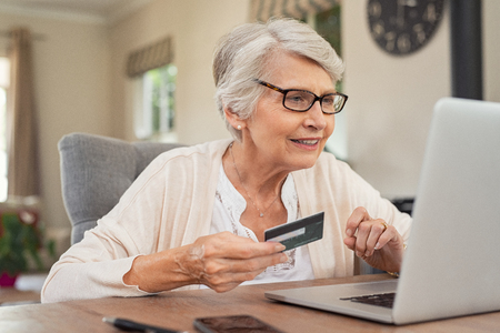 Happy senior woman making online payments using laptop. Smiling old grandmother doing shopping on ecommerce with credit card. Pensioner holding debit card for internet banking.の写真素材