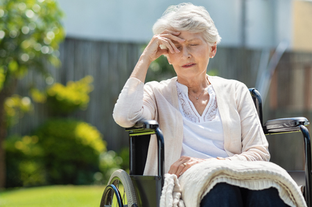 Sad senior woman sitting in wheelchair outside a nursing home. Depressed disabled lady with terrible headache. Solitude and abandon concept.の写真素材