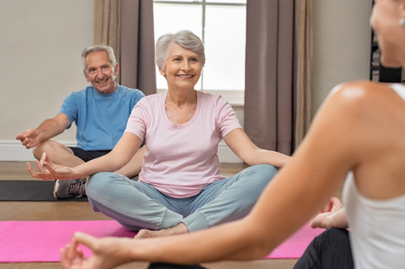 Senior couple with trainer sitting in lotus position meditating. Instructor with old man and elderly woman doing yoga at home. Fitness instructor helping old people keep fit.の写真素材