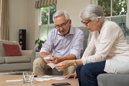 Smiling senior couple with papers, calculators and bills at home. Senior couple calculating taxes at home. Mature man and woman wearing spectacles and looking their expenses together.の写真素材