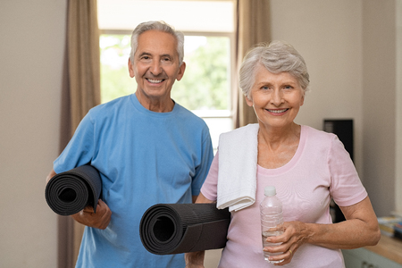Active healthy senior couple holding yoga mats while going together to training. Happy fitness elderly man and woman looking at camera. Portrait of old couple exercising together at home.の写真素材