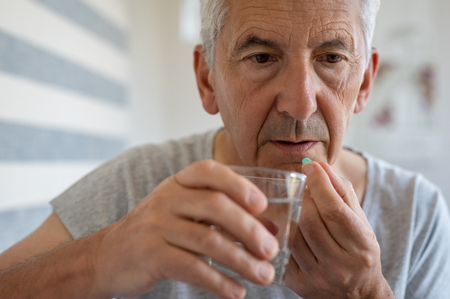 Ill senior man taking medicine for hypertension. Portrait of elderly man taking pills for depression. Old man swallowing pill with glass of water.の写真素材