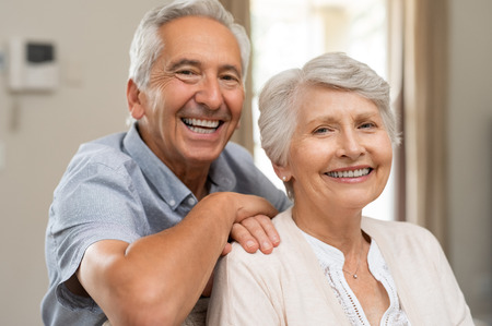 Portrait of happy healthy senior couple at home. Romantic old couple sitting together on sofa while looking at camera. Cheerful elderly wife and husband enjoying life after retirement.の写真素材