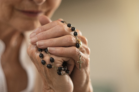 Old wrinkled hands holding a rosary. Closeup of christian senior woman hands holding rosary beads and crucified cross while praying God. Mature catholic lady holding black rosary and praying.の写真素材