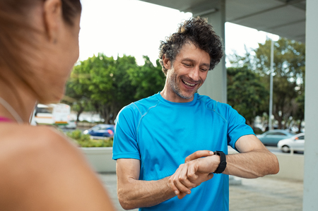 Mature jogger checking time on smart watch during running exercise. Smiling runner looking at smartwatch, checking gps position map. Happy fitness man checking heart rate monitor on wrist.の写真素材