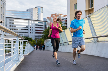 Happy man and beautiful woman jogging together city bridge. Healthy couple running on the city street. Middle aged couple running with building in the background.の写真素材