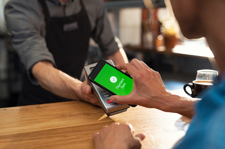 Customer paying bill through smartphone using NFC technology. Closeup of hand making payment through contactless machine. Woman hand holding mobile phone with green screen and paying the bill with contact less technology.の写真素材