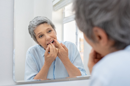 Mature beautiful woman cleaning her teeth with floss in bathroom.の写真素材