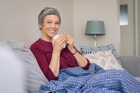 Portrait of smiling senior woman drinking coffee at home while looking at camera.の写真素材