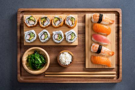 Top view of delicious variety sushi pieces setting on wooden tray. High angle view of japanese food with huramaki, maki, rolls, nigiri, seaweed and rice in a bowl. Flat image of fresh japanese sushi served on bamboo tray with chopstick on slate table.の写真素材