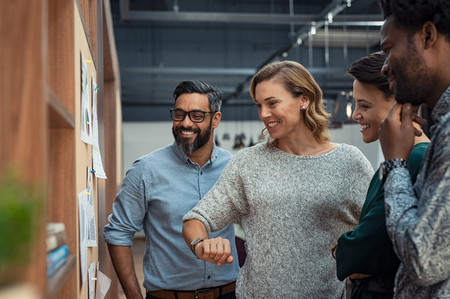 Group of mature businesspeople planning business strategy while looking at infographic displayed on wall. Business men and casual women looking at pie charts. Successful startup partners feeling happy on seeing progress in charts.の写真素材