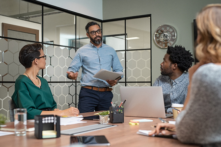 Confident mature businessman giving a presentation to his team in office. Business brief with annual goals with employees and mature boss in meeting room. Multiethnic leader training businessmen and businesswomen in conference room.の写真素材