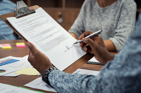 Closeup of african american businessman signing a contract during meeting. Hands of black man holding contract on clipboard reading and signing document. Man approving loan documents with team.の写真素材