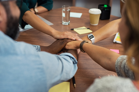 Multiethnic business people join hands while meeting in office. Closeup of successful group of businesspeople putting hands together. Unity, cooperation and teamwork concept.の写真素材