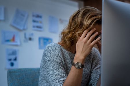 Portrait of tired business woman working at computer. Stressed casual businesswoman having headache at work. Overworked woman working late at night and holding her head in hands.の写真素材