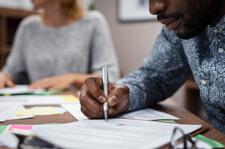 Closeup of businessman hand signing on formal paper during a meeting in boardroom. African american business man signing a contract. Closeup of a businessperson sign contract and making a deal.の写真素材