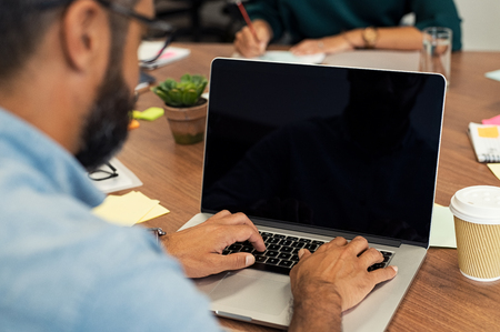 Back view of businessman sitting in front of laptop screen. Businessman typing on laptop in office.  Multiethnic casual man typing on empty screen computer sitting at wooden table.の写真素材