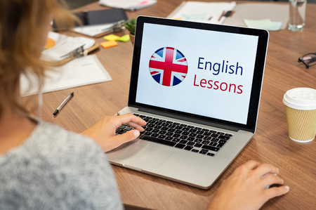 Mature woman learning English online with computer at office. Laptop screen of woman displaying english lessons poster with British flag. Closeup of student using laptop doing online course on english.の写真素材