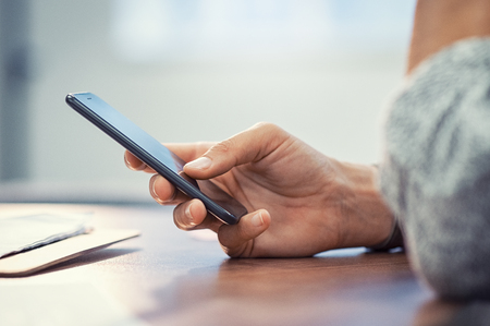 Closeup hand of woman using smartphone on wooden table. Businesswoman typing text message on smart phone. Casual lady hand holding mobile phone with blank screen at office.の写真素材