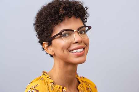 Beautiful young brazilian woman with spectacles looking at camera. Cheerful toothy smile girl with eyewear against grey background looking at camera. Portrait of casual african woman with new eyeglasses smiling.の写真素材