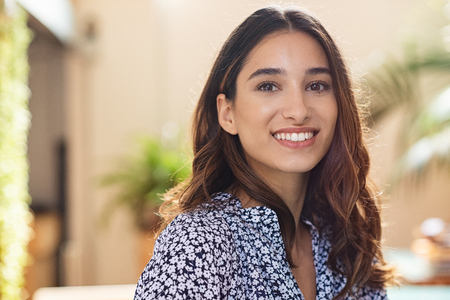Closeup face of happy smiling young woman. Portrait of beautiful latin girl looking at camera. Confident casual girl sitting at cafeteria.の写真素材
