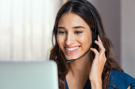Smiling woman using laptop while talking to customer on phone. Consulting corporate client in conversation with customer using computer on desk. Service desk consultant talking in a call center and working on laptop.の写真素材