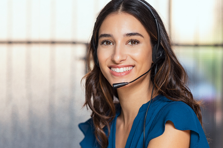 Customer support woman smiling and looking at camera. Portrait of happy customer support phone operator at call center wearing headset. Cheerful executive at your service working at office.