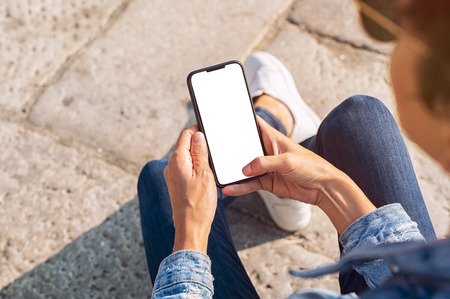 Closeup of young woman hand holding mobile phone with blank screen. Top view of girl using smartphone sitting on the stairs outside. High angle view of african woman unlocking cellphone while pressing home button.の写真素材