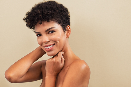 Beautiful young woman touching her face skin and feel the softness with copy space. Smiling brazilian girl feeling skin face after beauty treatment. Portrait of cheerful african woman isolated on background looking at camera.の写真素材