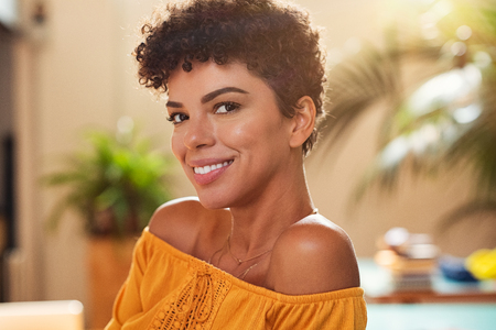 Portrait of natural beautiful girl smiling and looking at camera. Closeup face of brazilian young woman with curly hair. Charming african woman sitting at cafeteria.の写真素材