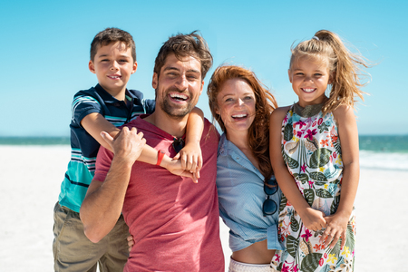 Portrait of happy family looking at camera at beach on a sunny day. Cheerful mother and father with cute daughter and son at sea during weekend. Smiling family with two children enjoying vacation at beach.の写真素材
