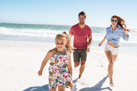 Happy family playing on the beach. Beautiful daughter running on the beach with mother and father in a bright sunny day. Smiling young family in casual having fun at sea.の写真素材
