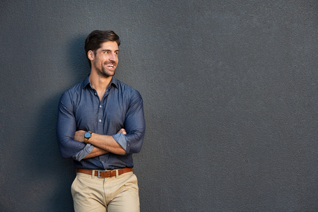 Happy successful businessman in smart casual clothing looking away. Portrait of satisfied business man with crossed arms isolated over grey background with copy space. Handsome young man smiling against grey wall.の写真素材