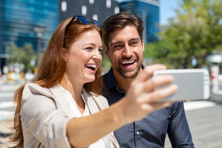 Young couple in love taking selfie with smartphone during trip. Newly wed husband and wife at honeymoon taking pictures. Smiling man and beautiful woman taking photo with smart phone.の写真素材