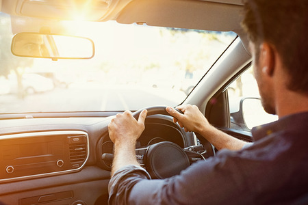 Rear view of young man looking straight while driving a car. Business man driving on the road. Back view of guy in formal clothing sitting on driver seat. Traveling for business work.の写真素材