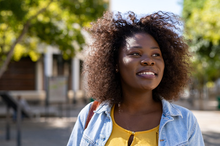 Portrait of curvy african woman thinking while looking away on the street. Closeup face of beautiful young african american woman smiling. Cheerful casual student girl with curly hair enjoying summer.の写真素材