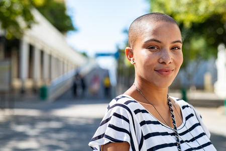 Portrait of young happy bald woman on city street looking at camera. Confident stylish girl outdoor with copy space. Proud and satisfied black curvy woman standing on street.の写真素材