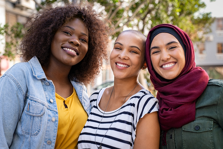 Group of three happy multiethnic friends looking at camera. Portrait of young women of different cultures enjoying vacation together. Smiling islamic girl with two african american friends outdoor.の写真素材