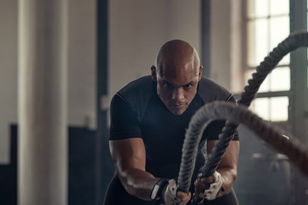 Man in sportswear doing battle ropes functional training at crossfit centre. Determined trainer...