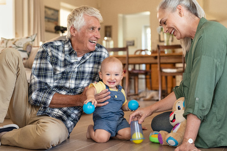 Smiling grandchild with grandparents playing with balls at home. Happy grandson with grandmother and grandfather playing with toys on floor at home. Senior woman and old man playing with little cute boy.の写真素材