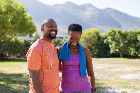 Cheerful black couple resting together after jogging in the park. Happy mature man and beautiful woman laughing while resting after running. Smiling woman and man taking a break after fitness training, copy space.の写真素材