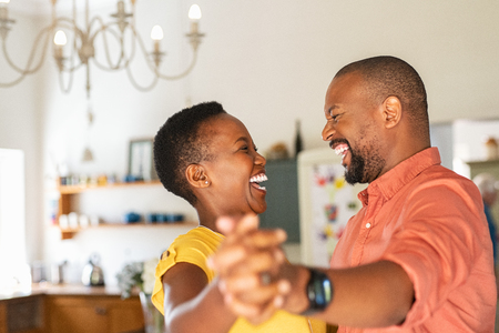 Cute mature couple dancing at home for their anniversary. Happy black woman enjoying a dance in the arms of her husband. Happy african couple dancing together in the kitchen and having fun together.の写真素材