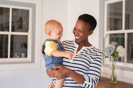 Portrait of happy black mother holding cute toddler laughing together at home. Cheerful african woman cuddling smiling little boy in hand and playing. Mature black nanny playing with little boy.の写真素材