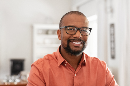 Smiling mature man wearing spectacles looking at camera. Portrait of black confident man at home. Successful entrepreneur feeling satisfied.の写真素材