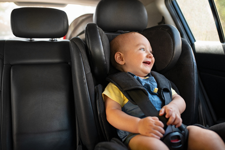 Portrait of cute smiling toddler sitting in car seat and looking outside the window. Little boy sitting in safety chair and laughing alone with copy spce. Happy child having fun in safety car seat while enjoy the travel.の写真素材