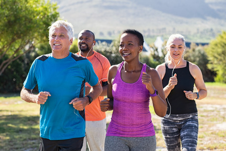 Healthy group of mature people jogging on track at park. Happy senior couple running at park with african friends. Multiethnic middle aged friends exercising together outdoor.の写真素材