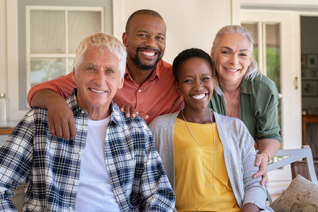 Senior couple with mature man and african woman posing for a photo sitting at courtyard. Portrait of happy multiethnic people sitting on couch under patio. Cheerful men and beautiful women looking at camera.の写真素材
