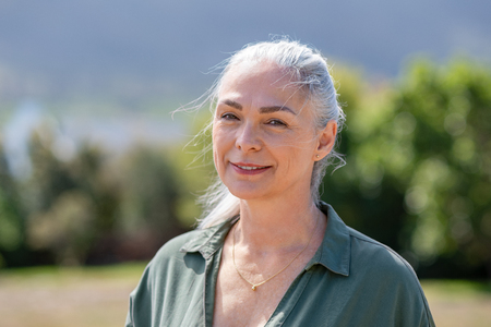 Closeup portrait of happy mature woman standing outside in summer. Portrait of smiling senior woman in garden. Active old woman with grey hair at park looking at camera with copy space.の写真素材