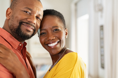 Portrait of romantic mature couple embracing at home and looking at camera. Smiling black man and woman together in new home. Closeup face of satisfied happy couple smiling in their new apartment with copy space .の写真素材